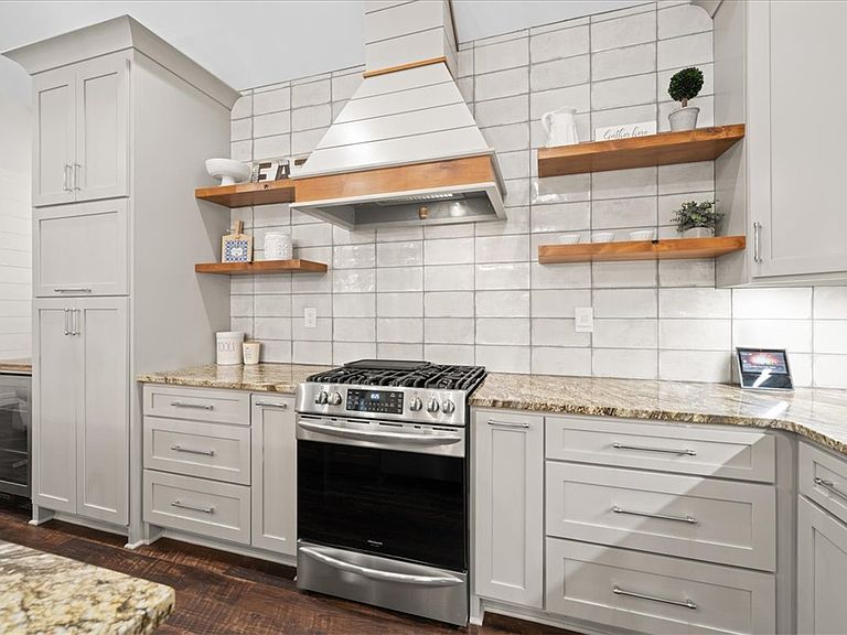 Close detail of the custom wood and white-plaster range vent hood at 107 Cedar Bluff Ct, with floating wood shelves on either side holding small plants and ceramics