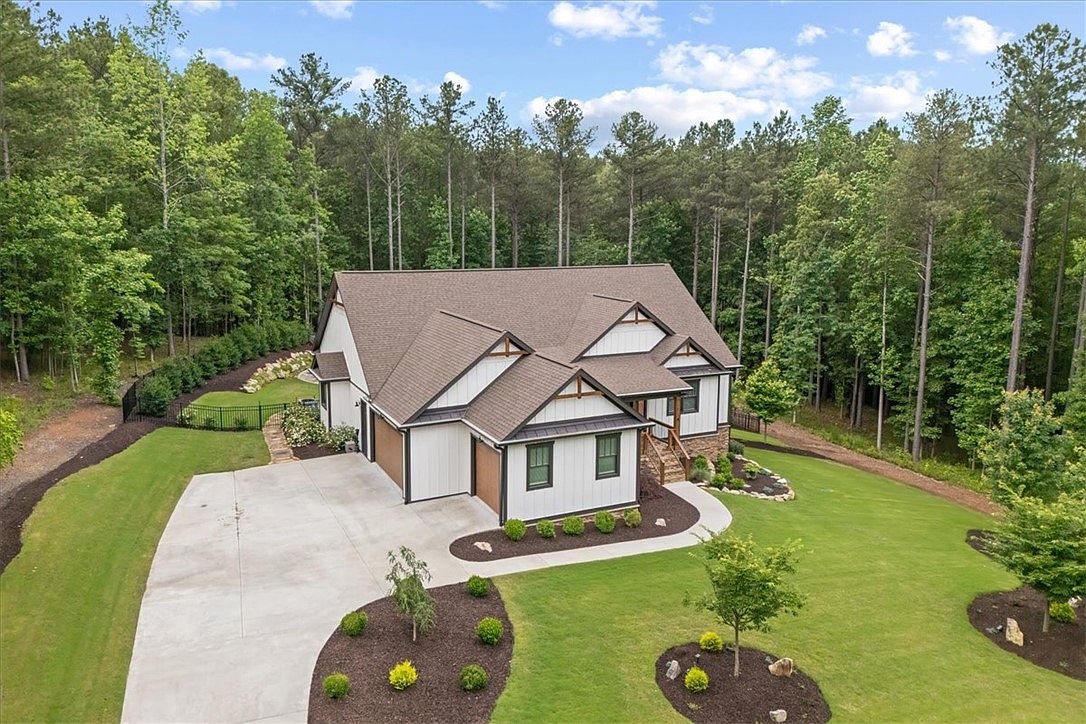 Aerial front view of 107 Cedar Bluff Ct, a 2021 modern farmhouse with white board-and-batten siding, dark gabled roofline, and three-car garage, held on 2.45 wooded acres near Six Mile, South Carolina